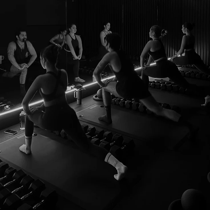 Functional training class holding a deep lunge along the dumbbell racks