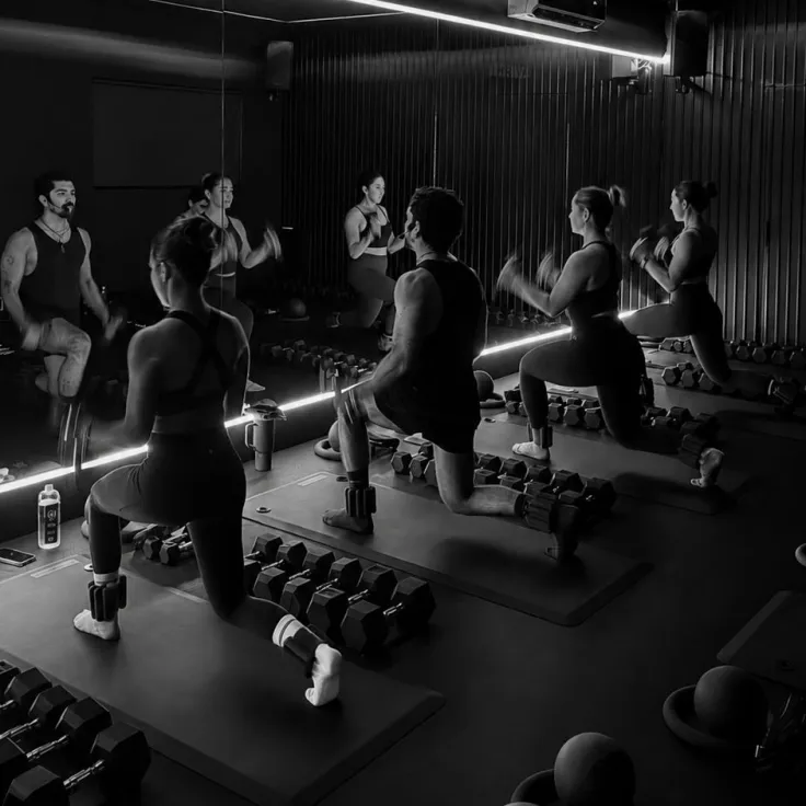 Sculpt class in the mirrored studio, holding a lunge over dumbbells
